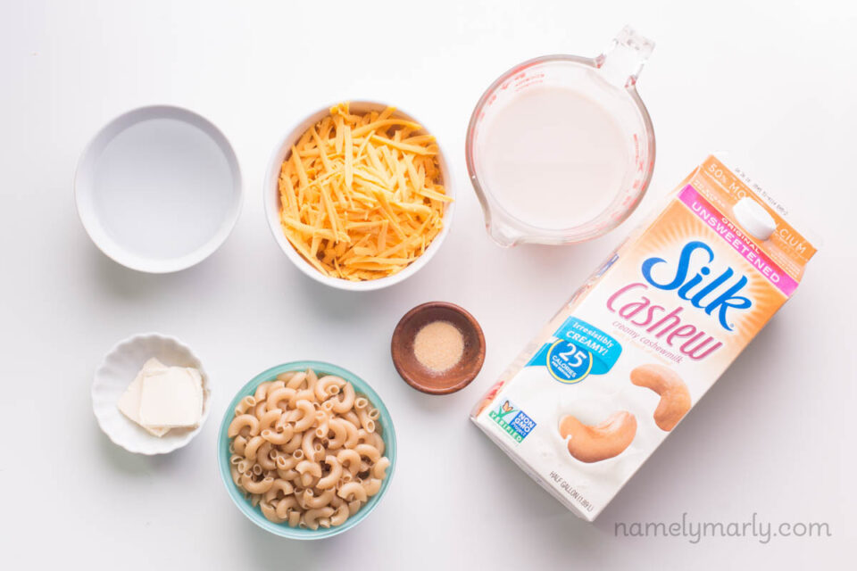 Looking down on ingredients to make vegan mac and cheese, including bowls of shredded vegan cheese, vegan butter, macaroni, and more.