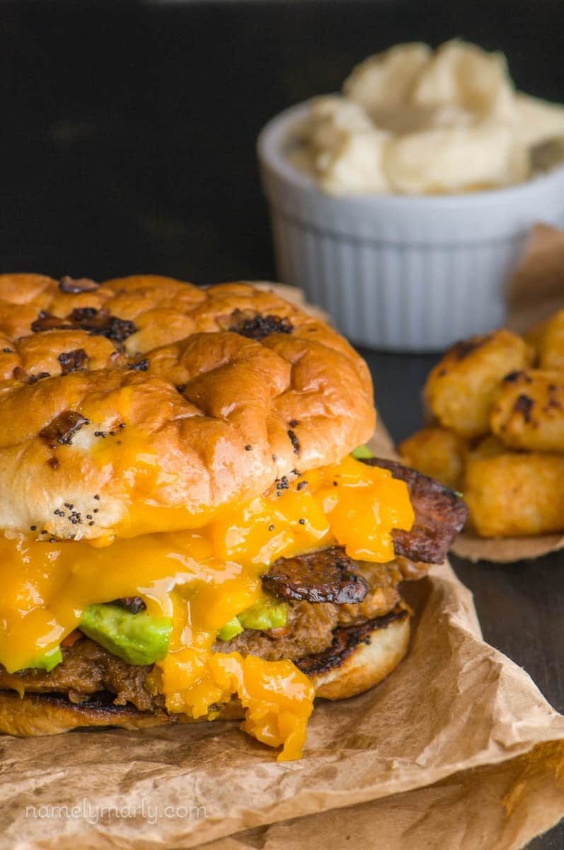 A close-up of the ultimate veggie burger, with melty vegan cheese showcased. There are tater tots and mayo behind it.