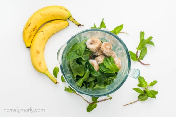 Spinach and bananas are in a blender jar. Next to it are more leaves of spinach and bananas.