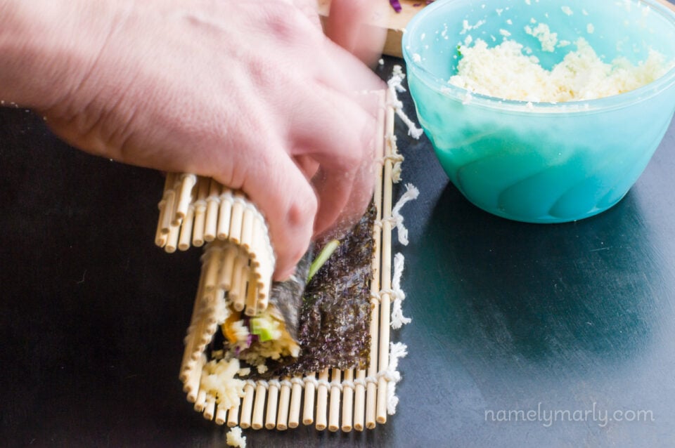 Hands finish rolling the sushi, using the bamboo mat.