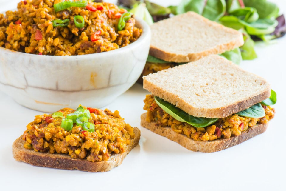 Several sandwiches made with vegan deviled ham spread sit beside a bowl with more of the spread.