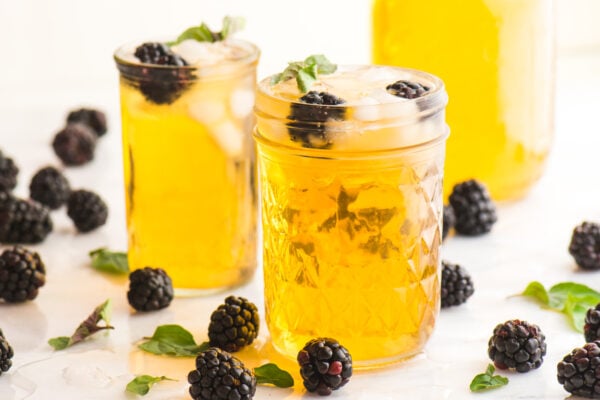 A closeup of two glasses of iced tea infused with blackberries and mint sprigs.
