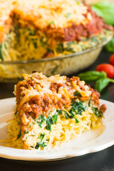 A plate of vegan spaghetti pie with melted vegan cheese on top sits on a dark countertop with the rest of the pie in the background.