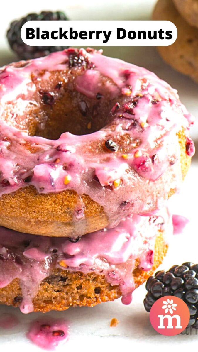 Stack of blackberry donuts topped with pink glaze, surrounded by fresh blackberries.