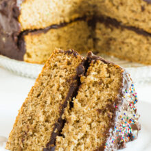 A slice of vegan vanilla wacky cake sits on a plate. The rest of the cake is behind it.