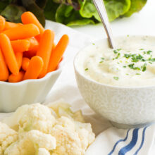 A bowl of vegan ranch dip has raw veggies sitting next to it.