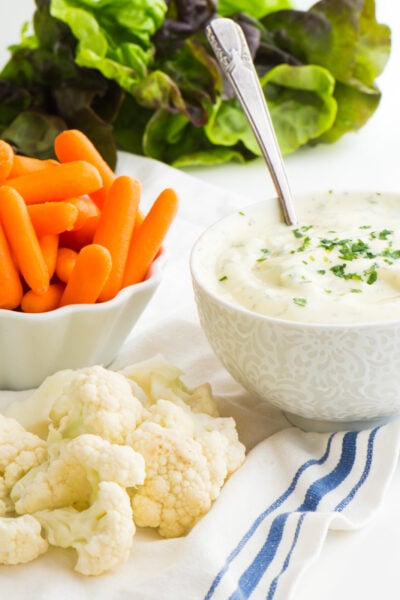 A bowl of vegan ranch dip has raw veggies sitting next to it.