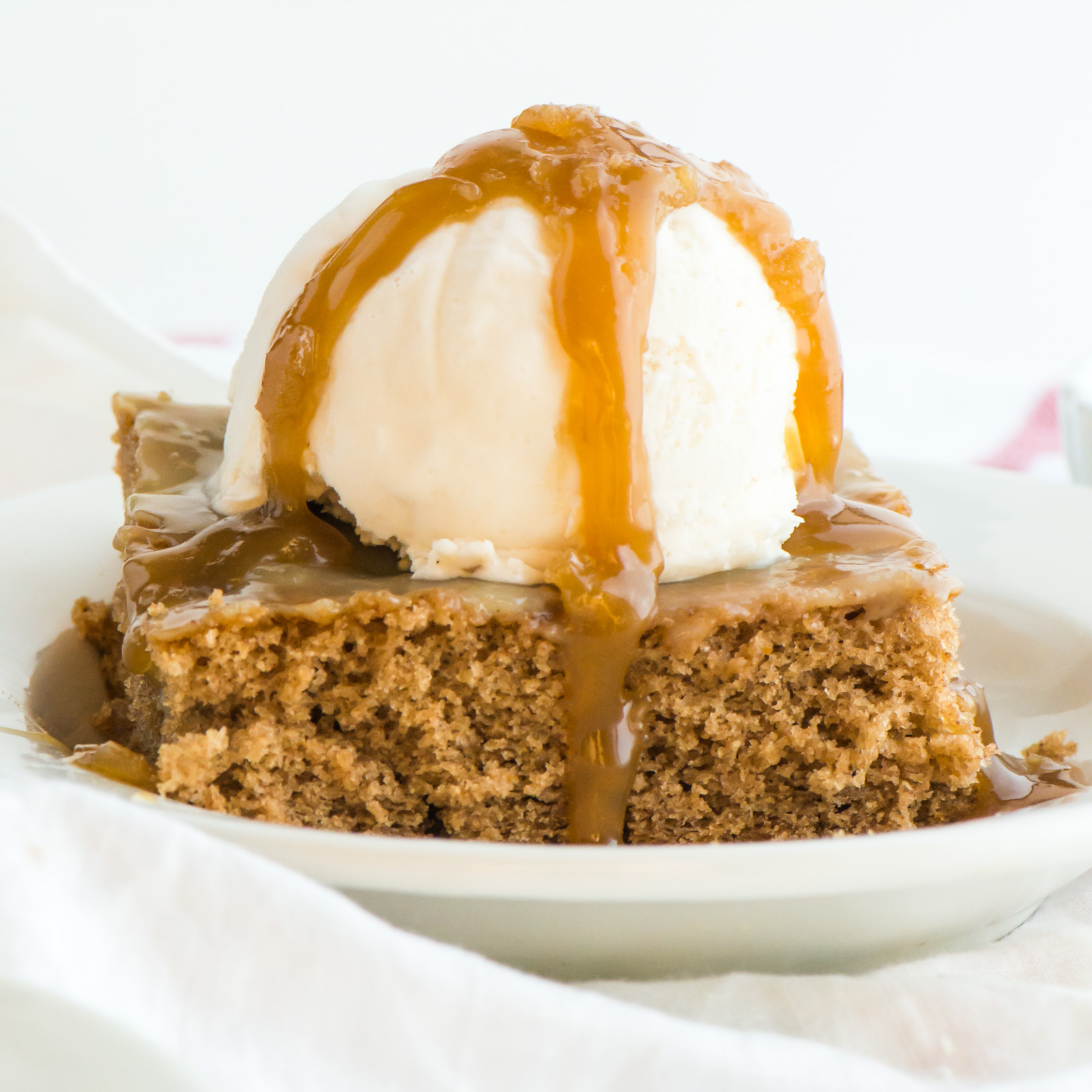 A slice of cake has a scoop of ice cream on top and drizzles of caramel sauce. 