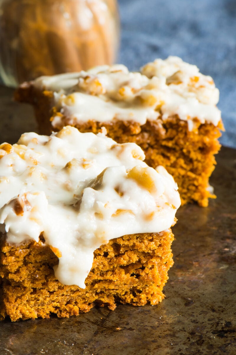 Two slices of vegan pumpkin blondies sit in front of a jar of cinnamon spice.