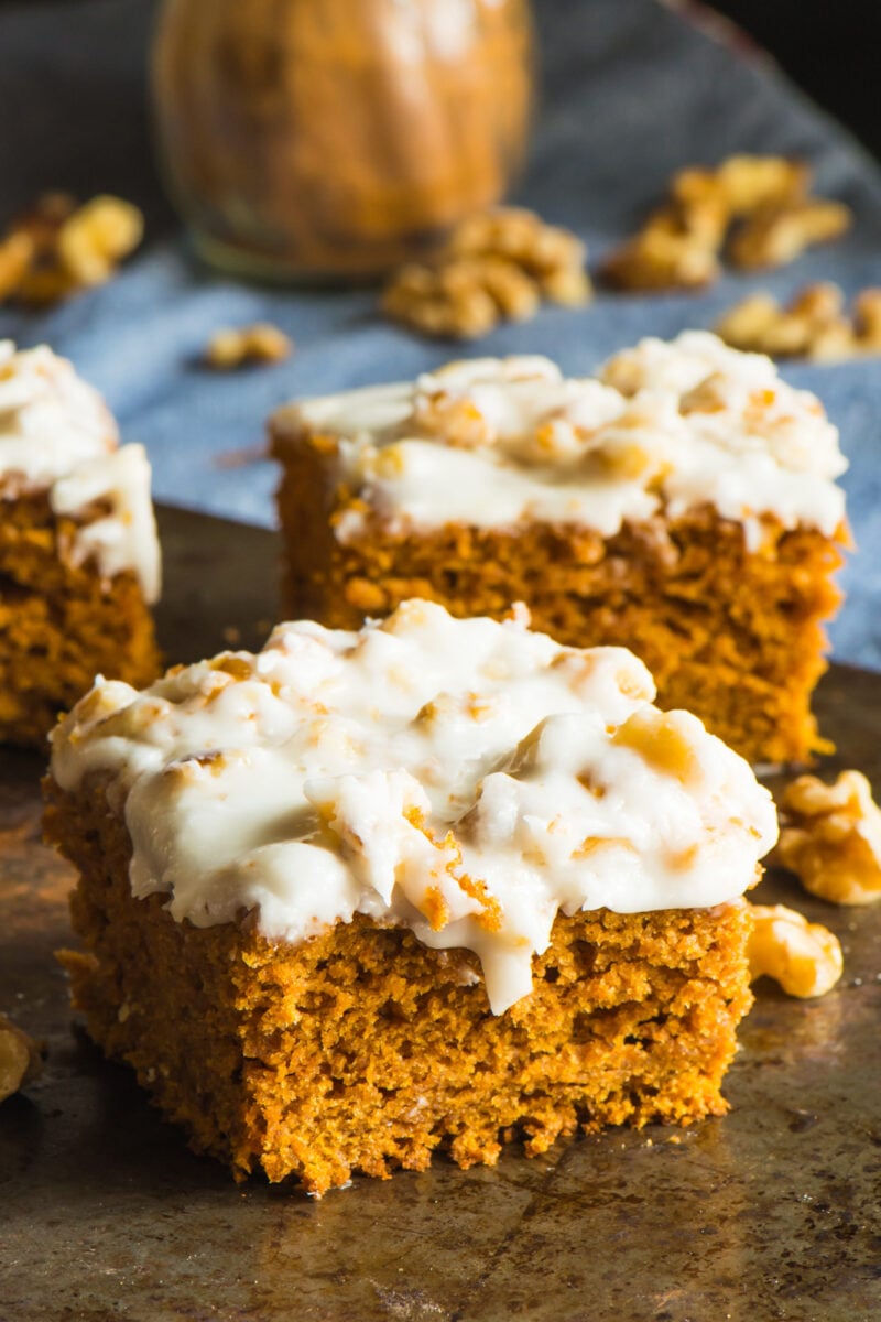Slices of vegan pumpkin blondies with chopped walnuts and a jar of cinnamon spice.