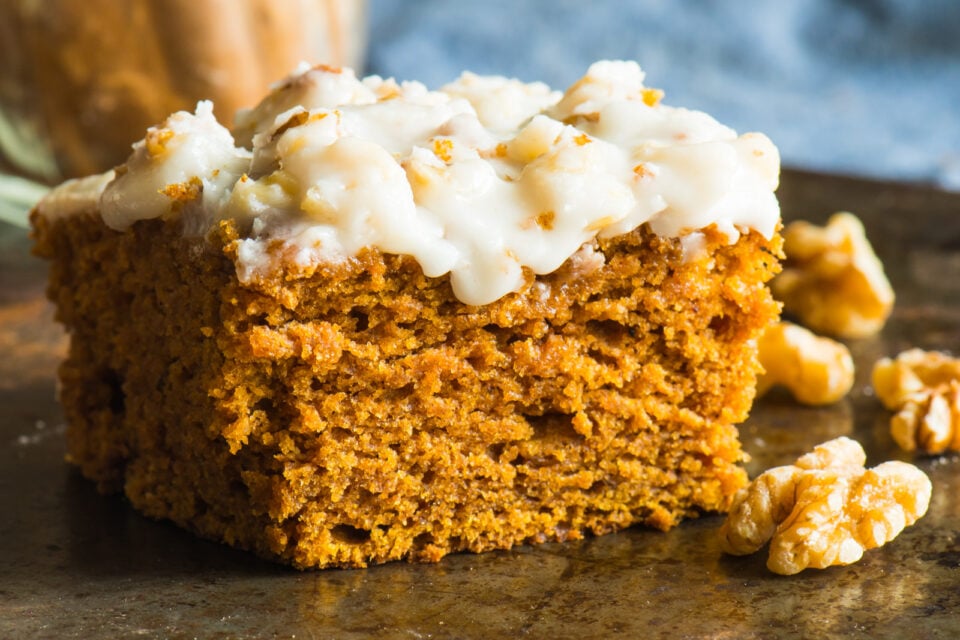 A slice of vegan pumpkin blondies with chopped walnuts beside it.