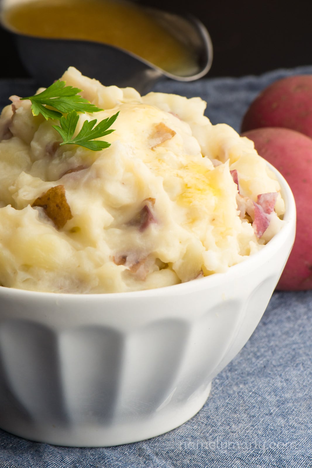 A bowl of mashed potatoes with a bowl of gravy behind it.
