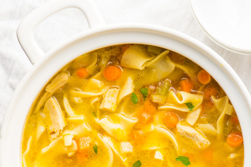 Looking down on a white pot full of vegan chicken noodle soup.