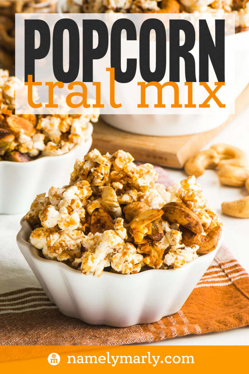 Bowl of popcorn trail mix with nuts, set on a striped napkin, with another bowl in the background.