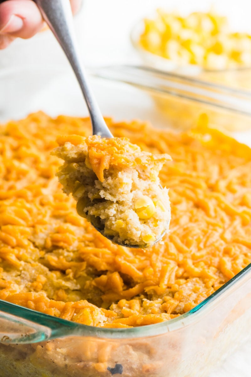A spoonful of vegan corn casserole hovers over the rest of the casserole dish.