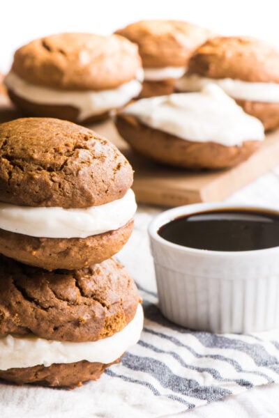 Two vegan gingerbread whoopie pies are stacked on top of each other sitting next to a bowl of syrup.