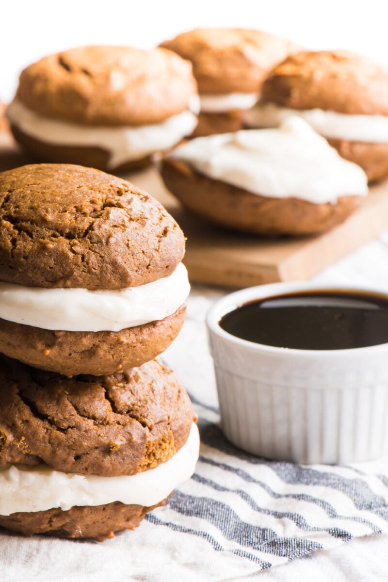 Two vegan gingerbread whoopie pies are stacked on top of each other sitting next to a bowl of syrup.