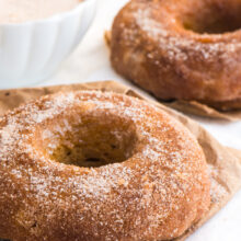 Vegan pumpkin cinnamon sugar donuts sit next to a bowl of cinnamon sugar.