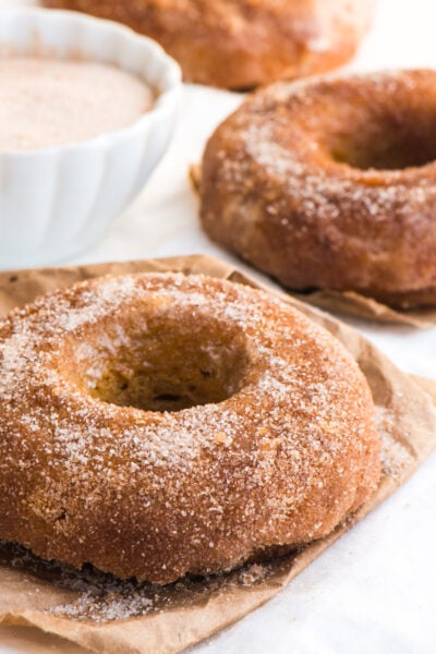 Vegan pumpkin cinnamon sugar donuts sit next to a bowl of cinnamon sugar.