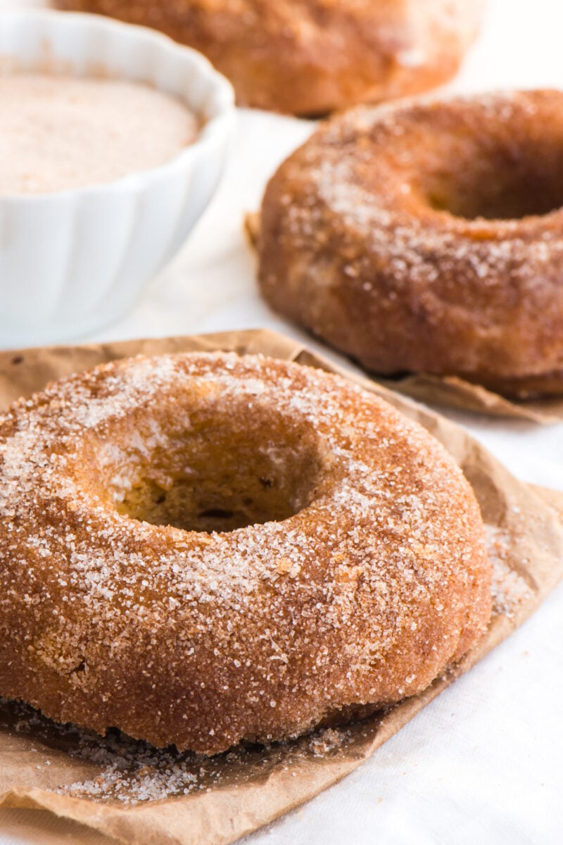 Vegan pumpkin cinnamon sugar donuts sit next to a bowl of cinnamon sugar.