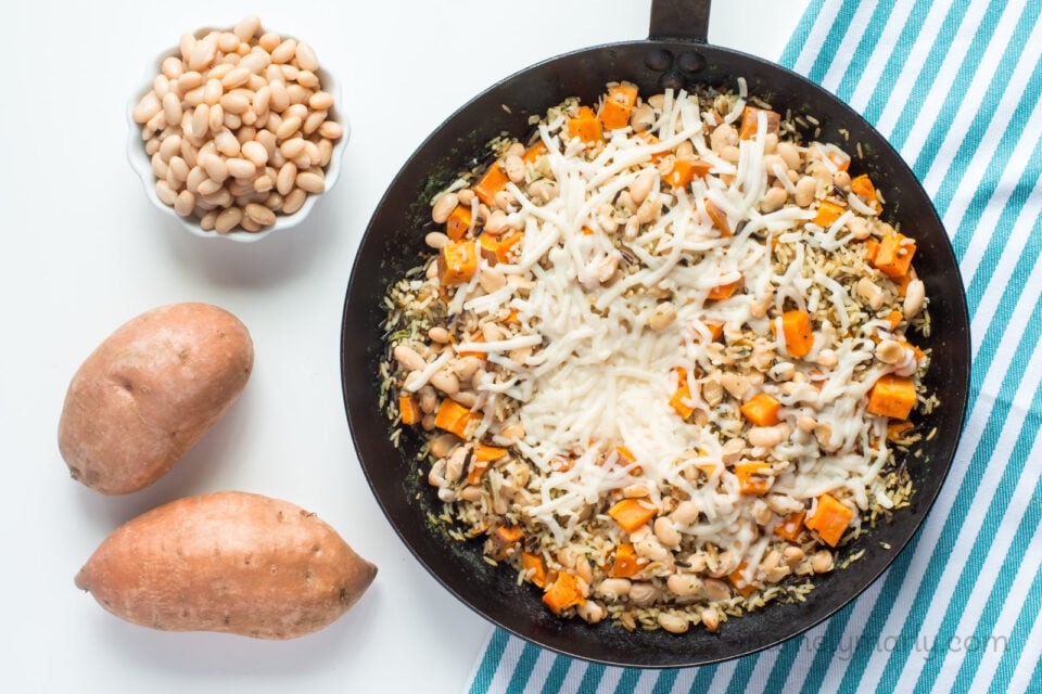 Looking down on ild rice and sweet potato skillet dinner in a skillet with a bowl of beans and sweet potatoes next to it.