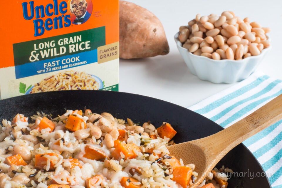 A close-up of a wooden spoon in skillet full of a rice and sweet potato skillet dinner with a bowl of beans behind it.