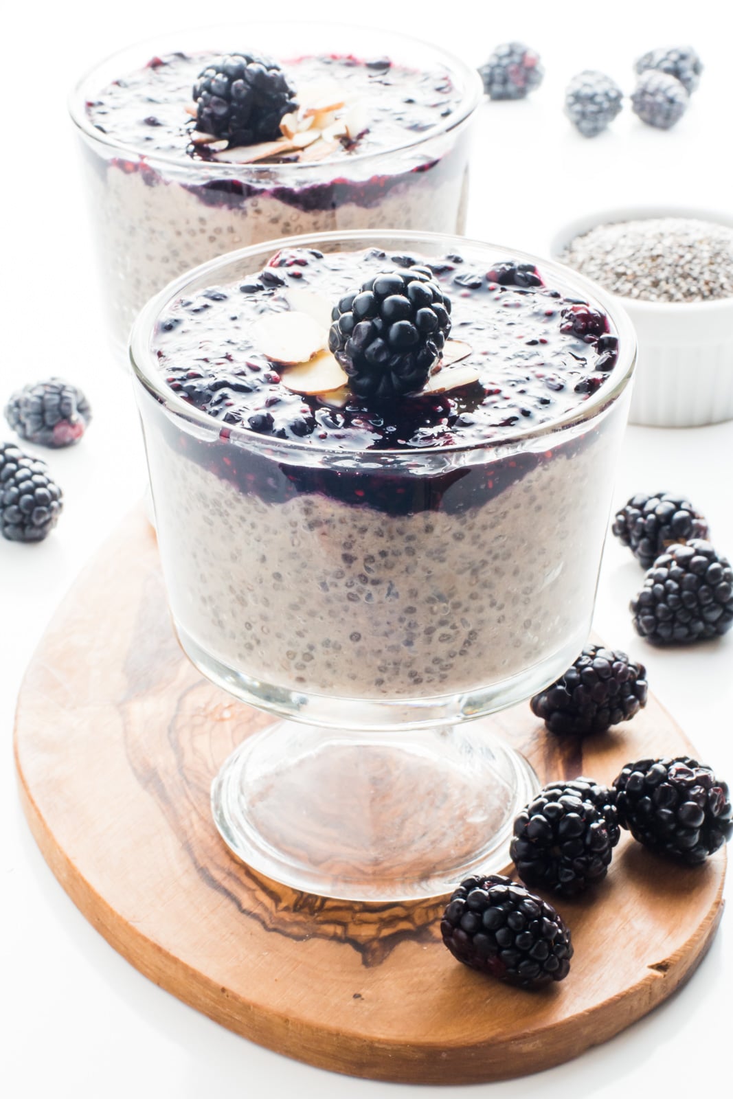 Vegan Banana Chia Pudding with Blackberry Sauce in a serving dish with another dish behind it and fresh blackberries around it.