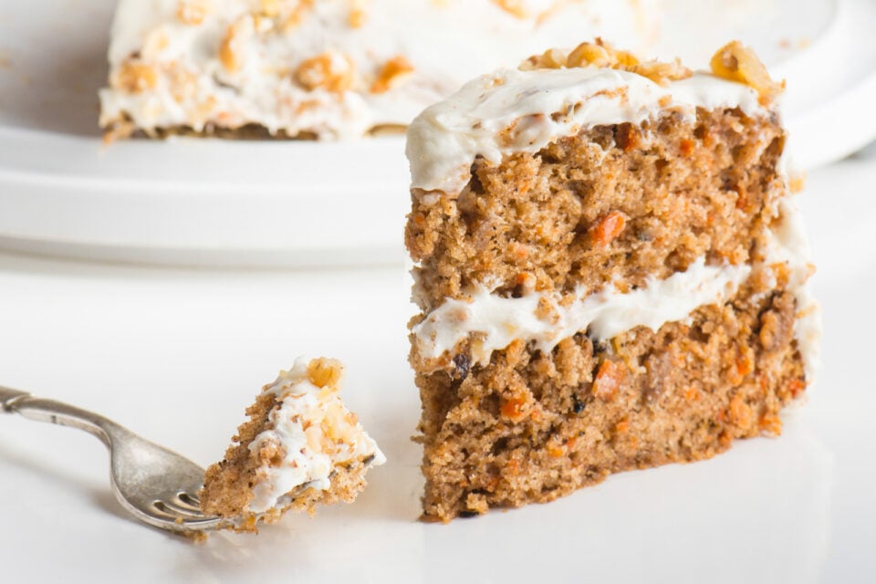 A slice of carrot cake has a fork sitting next to it with a bite of cake on the fork.