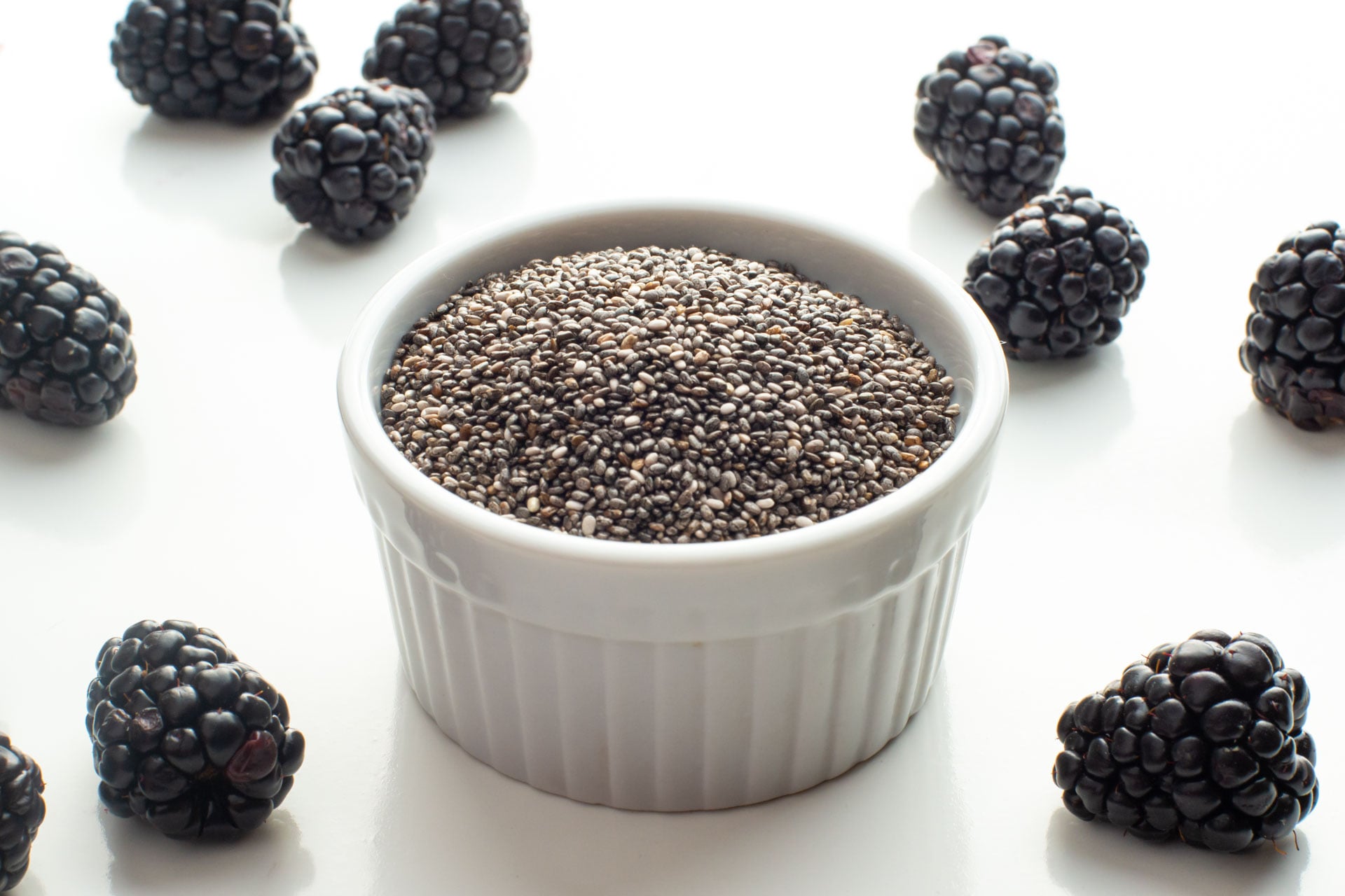 A small bowl of chia seeds sits next to fresh blackberries.