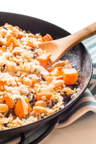 A skillet full of wild rice and sweet potato skillet dinner with a wooden spoon in it.