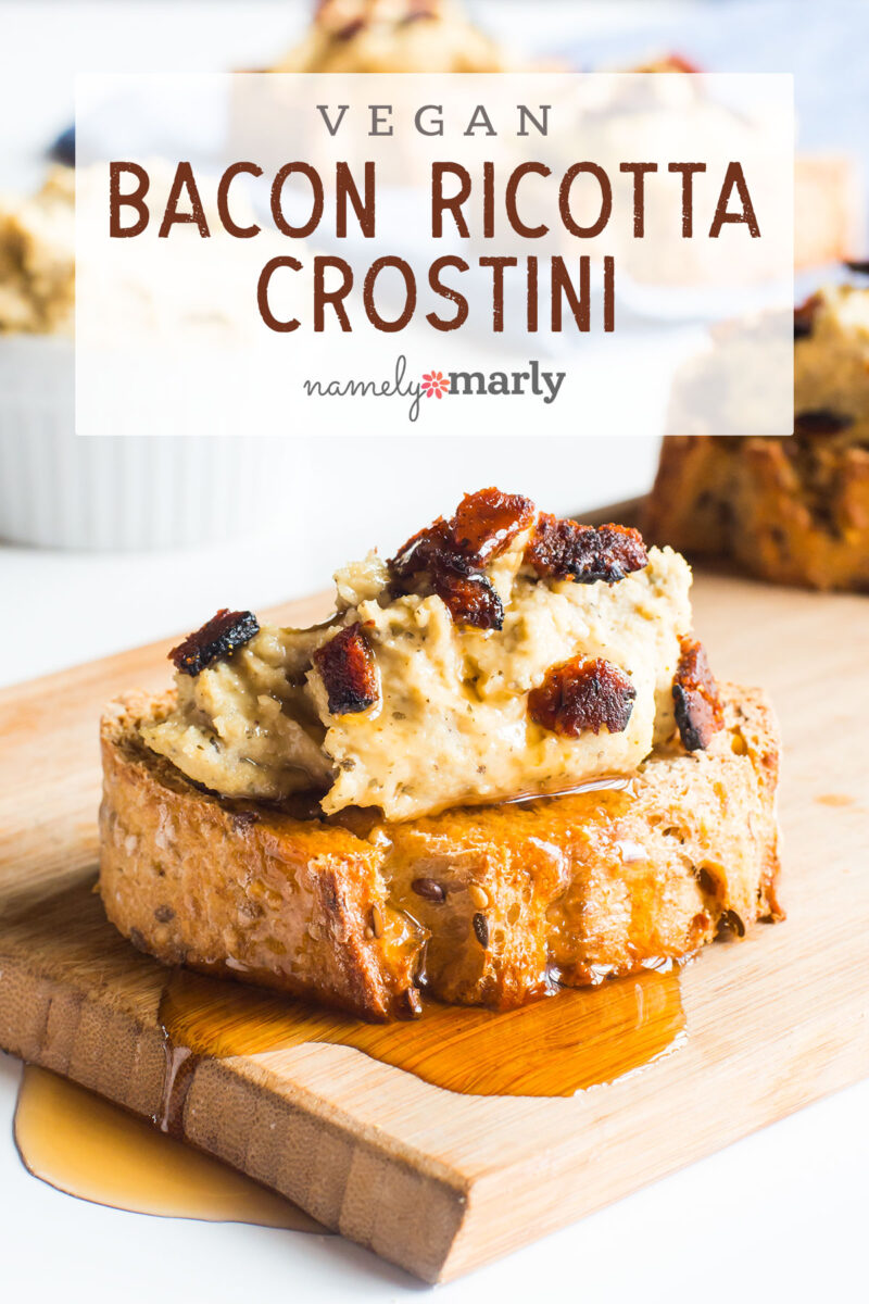 A slice of bread covered in vegan ricotta and vegan bacon bits sits on a wood cutting board