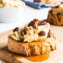 A slice of vegan bacon ricotta crostini with maple syrup drizzling over it on a cutting board.