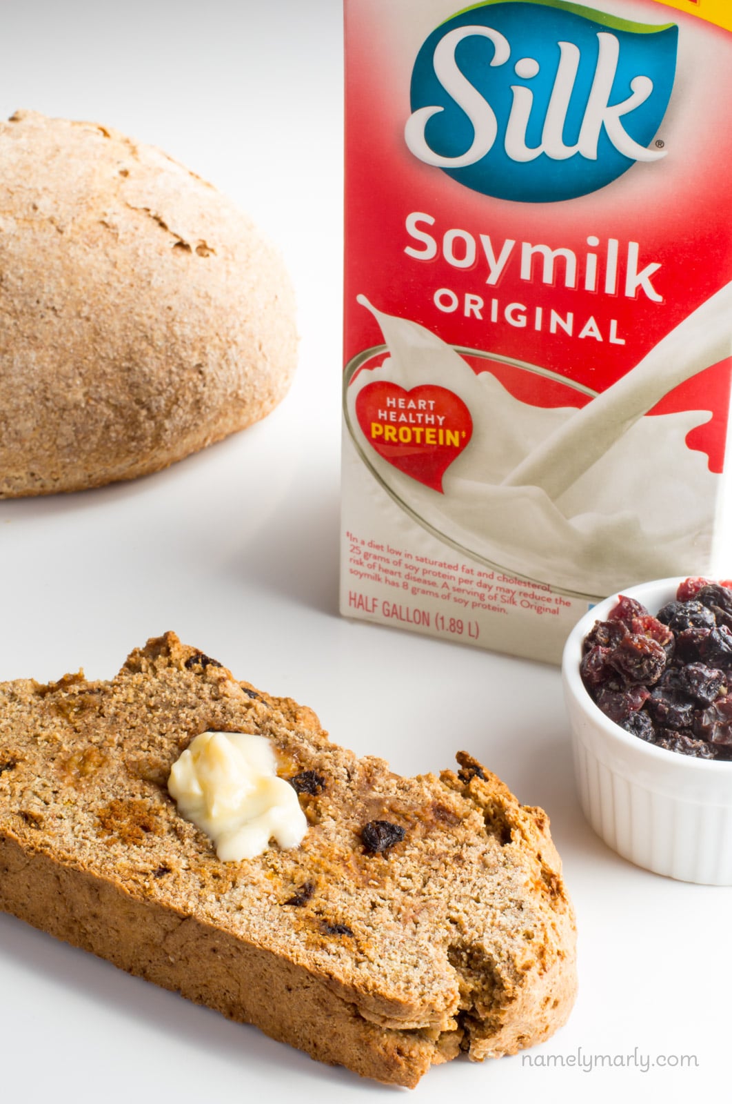 A slice of vegan Irish soda bread with butter on top sits next to dried cranberries.