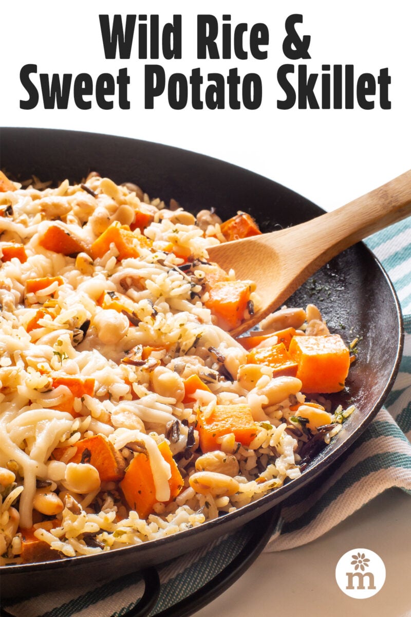 Wild rice and sweet potato skillet with vegetables topped with melted cheese in a cast iron pan.