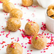 A group of Sugar Cookie Energy Bites sits on a white surface surrounded by red and pink heart-shaped confetti