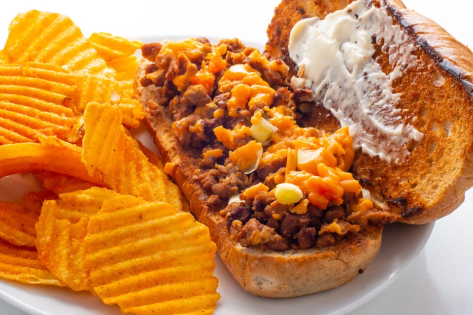A vegan chopped cheese sandwich on a plate next to potato chips.