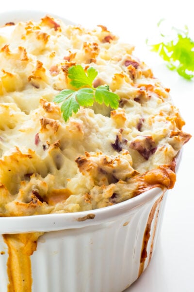 A casserole full of vegan shepherd's pie is on a white counter with fresh parsley around it.