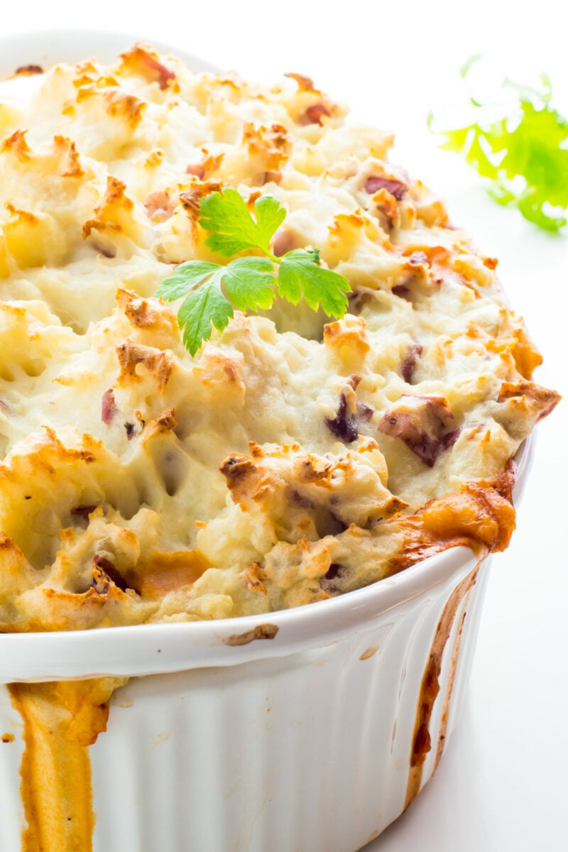A casserole full of vegan shepherd's pie is on a white counter with fresh parsley around it.