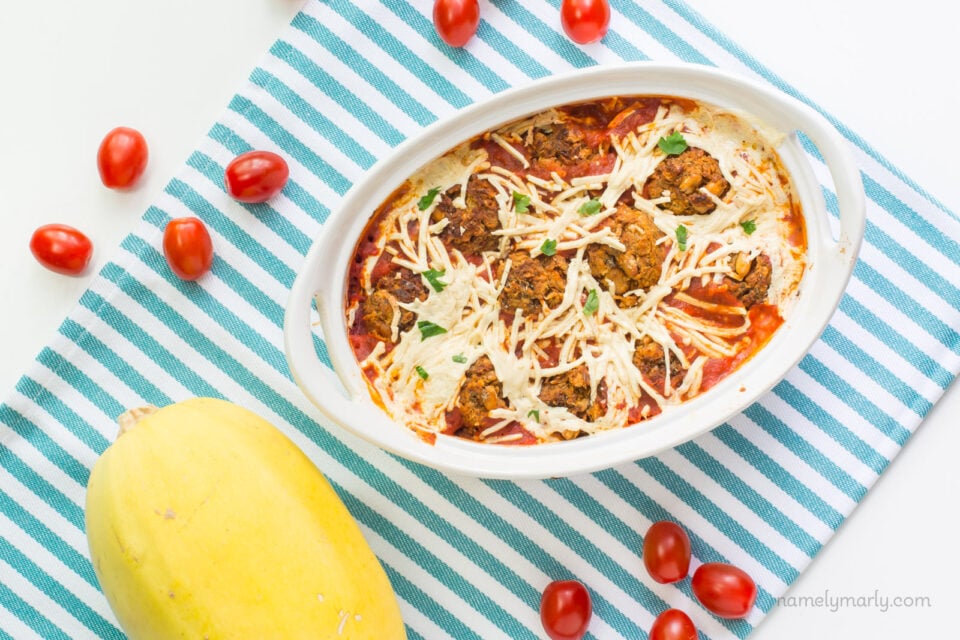 Looking down on a casserole with a spaghetti squash beside it and fresh cherry tomatoes around it.