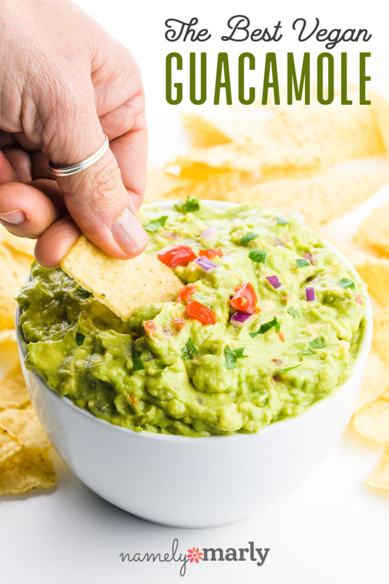 A hand holding a tortilla chip digs into a large bowl of guacamole with text that reads The Best Vegan Guacamole