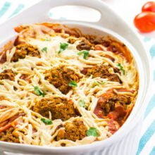 A casserole dish with vegan spaghetti squash and meatballs sits on a counter with fresh cherry tomatoes behind it.