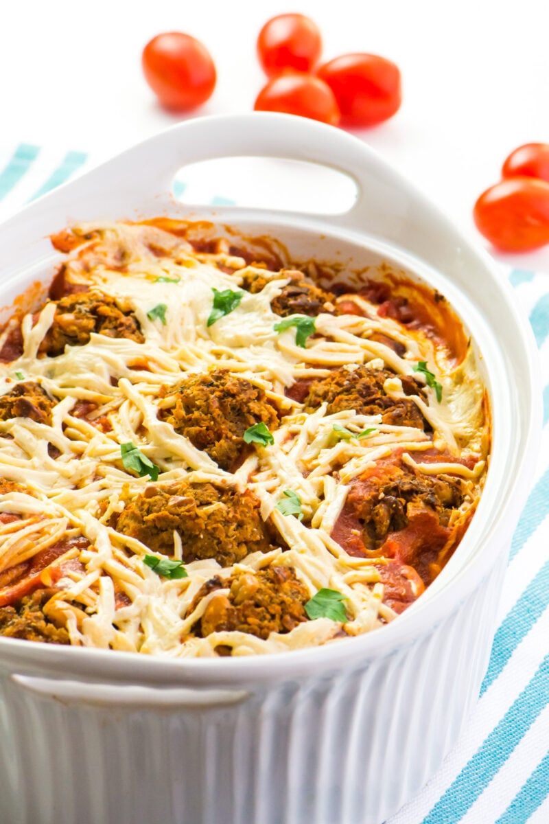 A casserole dish with vegan spaghetti squash and meatballs sits on a counter with fresh cherry tomatoes behind it.