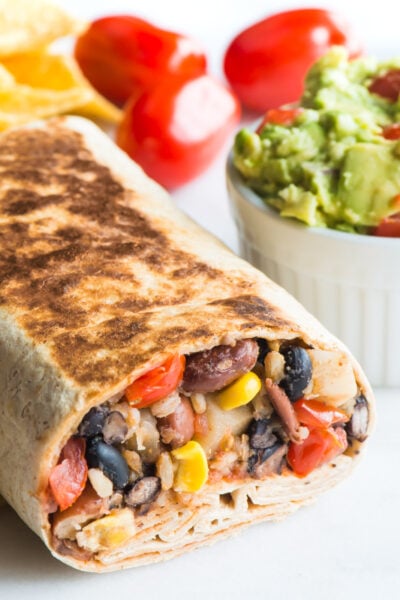 Crispy Black Bean Burrito sits next to a bowl of guacamole and fresh cherry tomatoes.