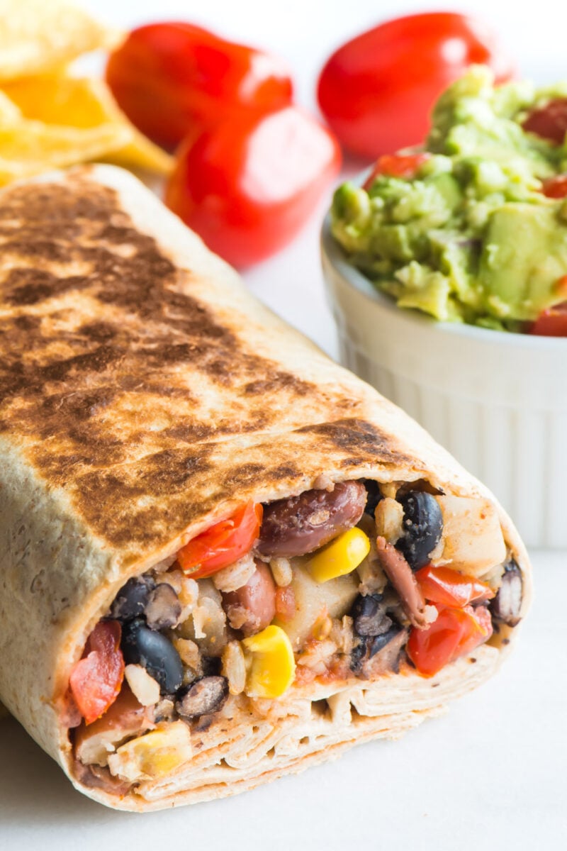 Crispy Black Bean Burrito sits next to a bowl of guacamole and fresh cherry tomatoes.