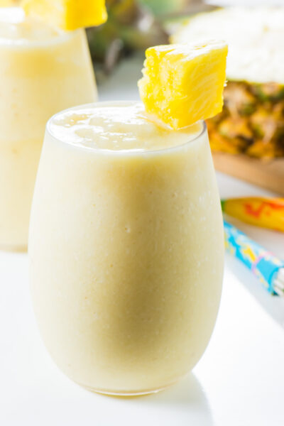 A pina colada cocktail has a piece of pineapple on the glass with a fresh pineapple behind it.