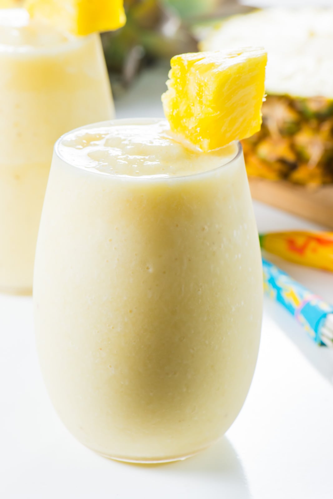A pina colada cocktail has a piece of pineapple on the glass with a fresh pineapple behind it.
