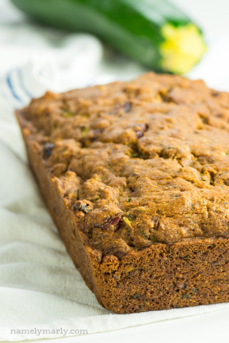 A loaf of zucchini bread sits in front of a zucchini.