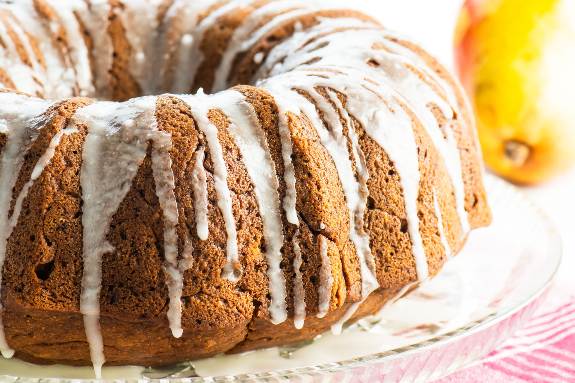 A bundt cake with white icing sits next to a pear.