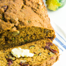 A loaf of vegan healthy zucchini bread with a slice cut off sits next to a zucchini.