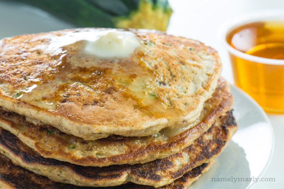 A stack of pancakes has melted butter on top and a bowl of syrup behind it.